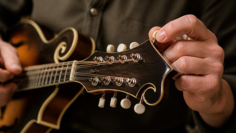 A person tuning a mandolin by adjusting the tuning pegs on the instrument's headstock.