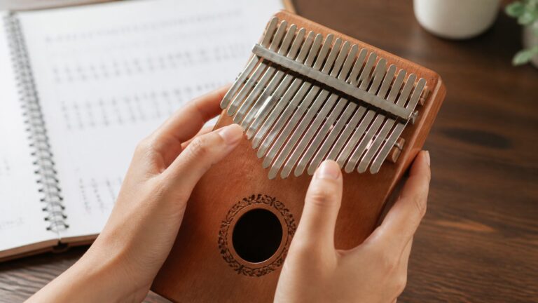 Close-up of hands playing a kalimba on a wooden table with a blurred background.