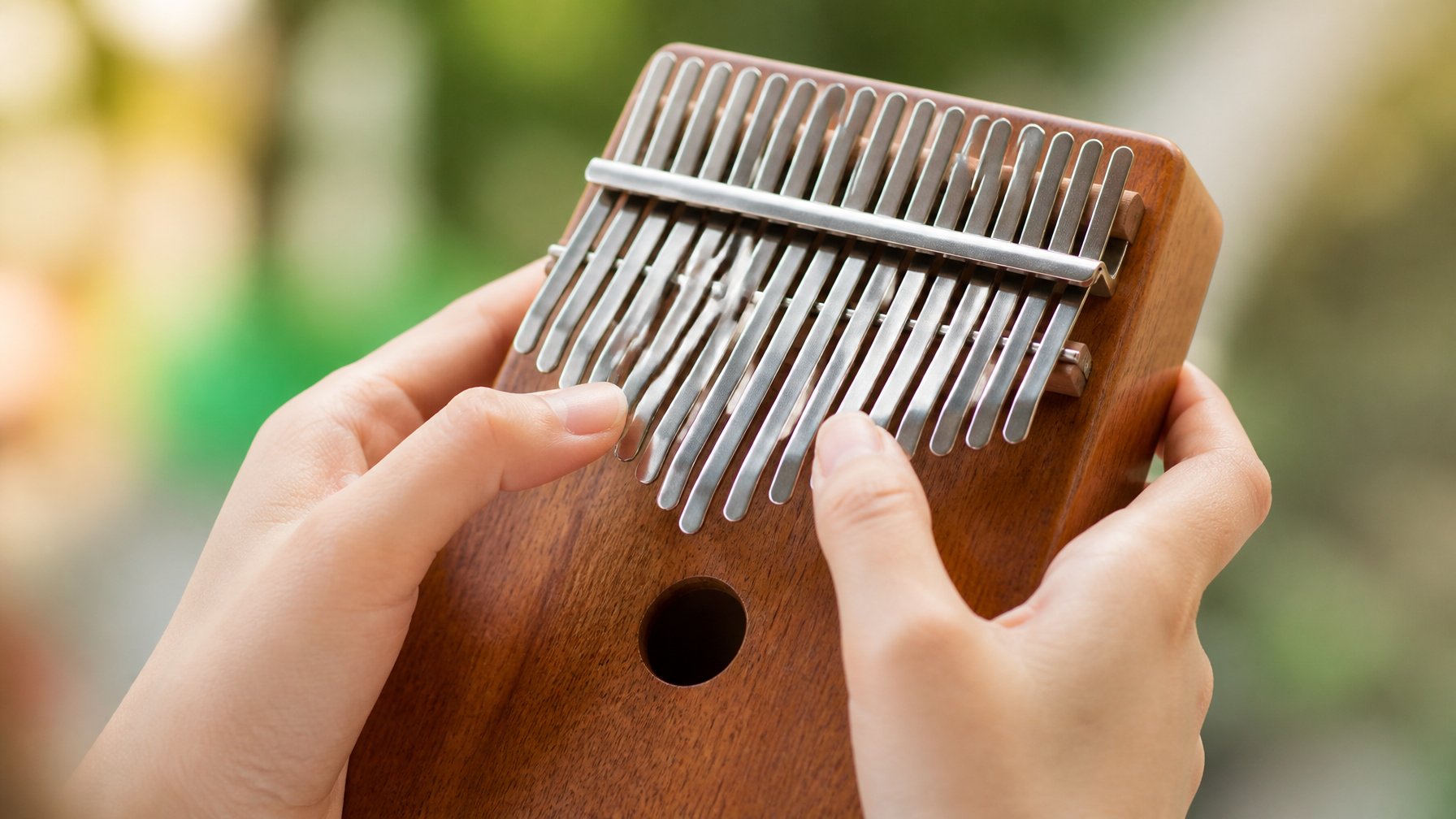 Close-up of hands playing a kalimba, focusing on the fingers pressing the metal tines.