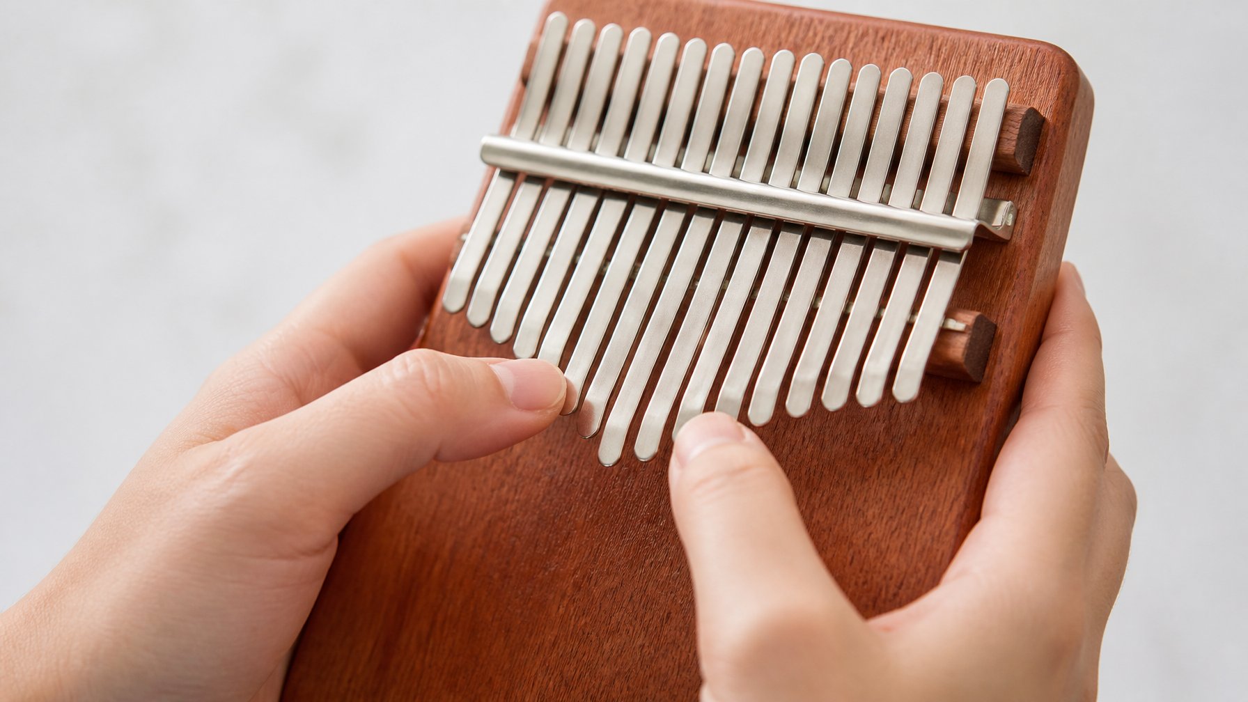 Close-up of hands playing a kalimba with metal tines in a well-lit indoor setting.