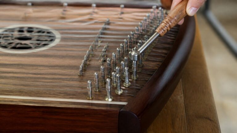 Close-up of a hammered dulcimer being tuned with a tuning hammer on a wooden table.